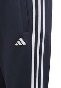 Pantalones deportivos de color navy con tres rayas blancas a lo largo del costado, fabricados con un material suave y elástico, con un logo de Adidas en el muslo.