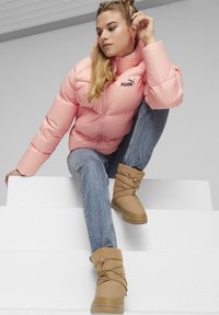 Puffjakke i blød pink med lynlås foran og logo; parret med brune, pelsforede ankelstøvler med samlet design. Blå skinny jeans.
