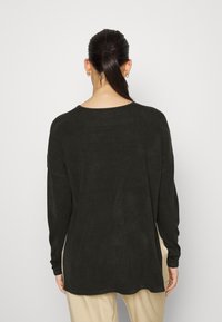 Czarny sweter z długim rękawem z okrągłym dekoltem i luźnym krojem. Materiał wydaje się miękki z delikatną teksturą. Obecne są rozcięcia po bokach.