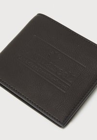 Cartera de cuero negro texturizado con el logotipo en relieve "Donataco2 Hermandad Canadiense" y símbolo de hoja de arce sobre un fondo blanco.