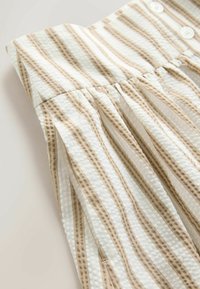 Close-up van wit en beige gestreepte gestructureerde stof met een geplooide naad en twee witte knopen op een kledingstuk tailleband.