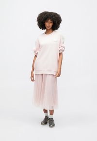 Světle růžová oversized mikina s texturovaným květinovým akcentem, kombinovaná s průsvitnou růžovou tylovou sukní. Nositelná s šedými sportovními botami a bílými ponožkami.