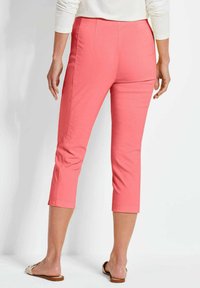 Koraalkleurige cropped broek gemaakt van lichtgewicht stof, met een platte tailleband, subtiele stiksels en zijsplitten aan de onderkant voor verbeterde beweging.