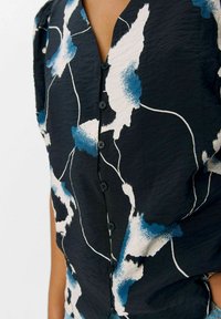 Blusa negra con un patrón floral abstracto en azul y blanco, escote en V, mangas cortas y botones negros en la parte delantera. Tela suave y texturizada.