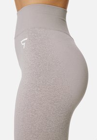 Hochtaillierte, hellgraue Leggings aus strukturiertem Material mit einem Farbverlaufmuster und einem kleinen Logo an der Hüfte. Figurbetontes Design.