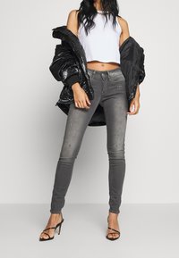 Chaqueta de plumas negra, top corto blanco, jeans ajustados grises con detalles desgastados y tacones altos negros con tiras.