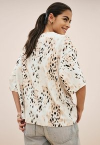 Volnější krátký rukáv v světlé béžové barvě s černým a hnědým leopardím potiskem. Hladký materiál, kulatý výstřih a postranní rozparky.