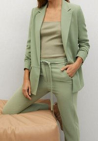 Blazer vert clair sur un haut côtelé, associé à un pantalon fuselé assorti. Texture douce avec taille à cordon de serrage et poches latérales.