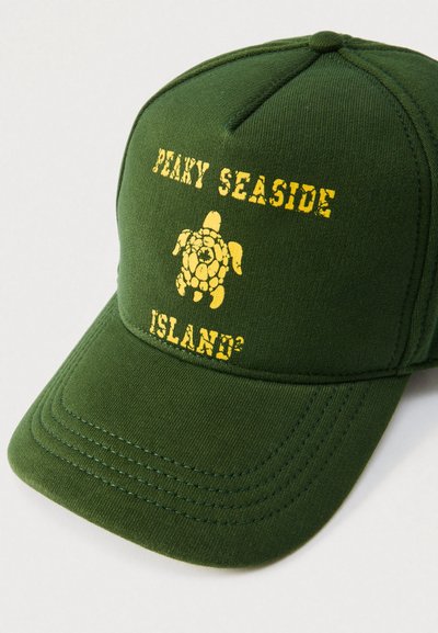 Grøn baseballkasket med en gul skildpaddegrafik og teksten "PEAKY SEASIDE ISLAND²" trykt på forsiden. Fremstillet af bomuld, struktureret design.