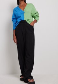 Suéter de punto con diseño dividido en azul y verde, con escote en V y ajuste holgado. Combinado con pantalones anchos negros. Textura suave.