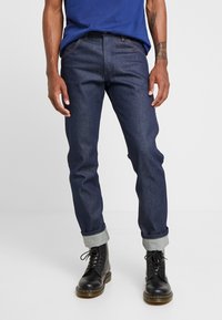 Mörkblå denimjeans med slim fit, med medelhög midja, uppvikta fållar och kontrasterande sömmar. Matchas med svarta snörkängor.