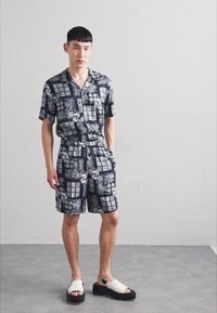 Short-sleeve shirt and shorts set, navy with floral patterns, lightweight fabric, relaxed fit, paired with chunky black sandals with white straps.