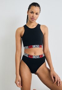 Top court noir et culottes taille haute en matériau lisse, affichant une marque "DIESEL" audacieuse en blanc et rouge sur les bandes élastiques.