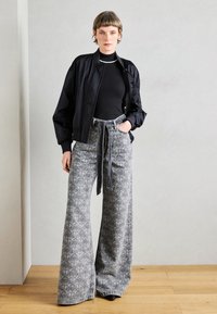 Black bomber jacket over a fitted black turtleneck, paired with high-waisted wide-leg gray patterned jeans featuring a tie belt.