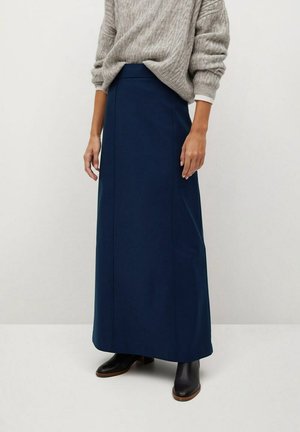Marineblå lang nederdel lavet af et glat stof, med en høj talje og lodrette sømdetaljer. Sammen med en lysegrå, ribbet sweater.