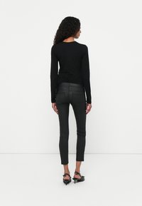 Zwart shirt met lange mouwen en een ronde hals, gecombineerd met strakke zwarte broek en zwarte hakken, zichtbaar stiksel en textuur.