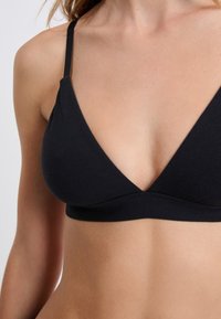 Brassière triangulaire noire avec bretelles ajustables fines et un tissu lisse et extensible. Sans rembourrage ni ornements, mettant en avant la simplicité du design.