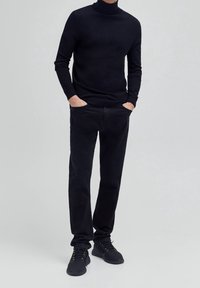 Schwarzer Rollkragenpullover kombiniert mit schwarzen Jeans und schwarzen Sneakers. Der Stoff scheint weich zu sein, mit einer figurbetonten Silhouette und ohne sichtbare Muster.