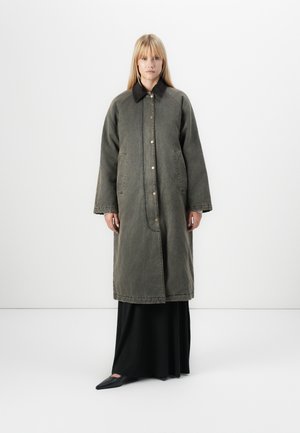 Oversized green denim coat with a black collar, featuring large pockets and front buttons, worn over a black floor-length dress.
