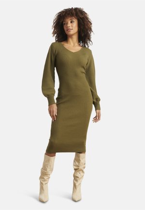 Olive green ribbed knit midi dress with a V-neck and long sleeves, paired with cream knee-high boots. Textured fabric, fitted silhouette.