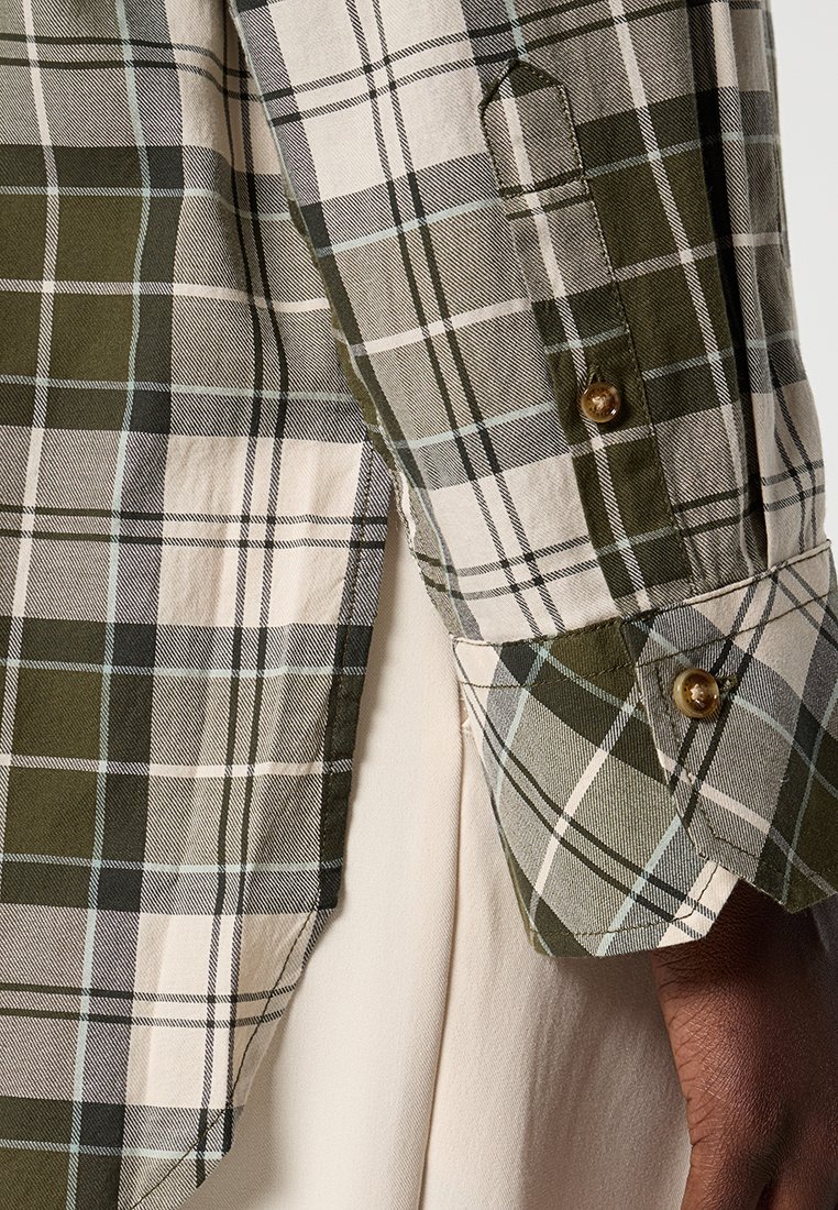 Camisa de cuadros verde y beige que presenta un puño con botón, patrones contrastantes y una tela texturizada. Los detalles incluyen botones dorados.