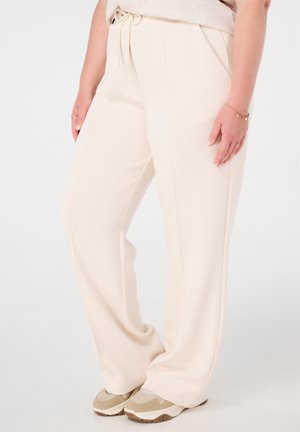Beige wijde broek gemaakt van zachte stof, met een verstelbare tailleband en zijzakken, gecombineerd met tan kleurige sportschoenen.