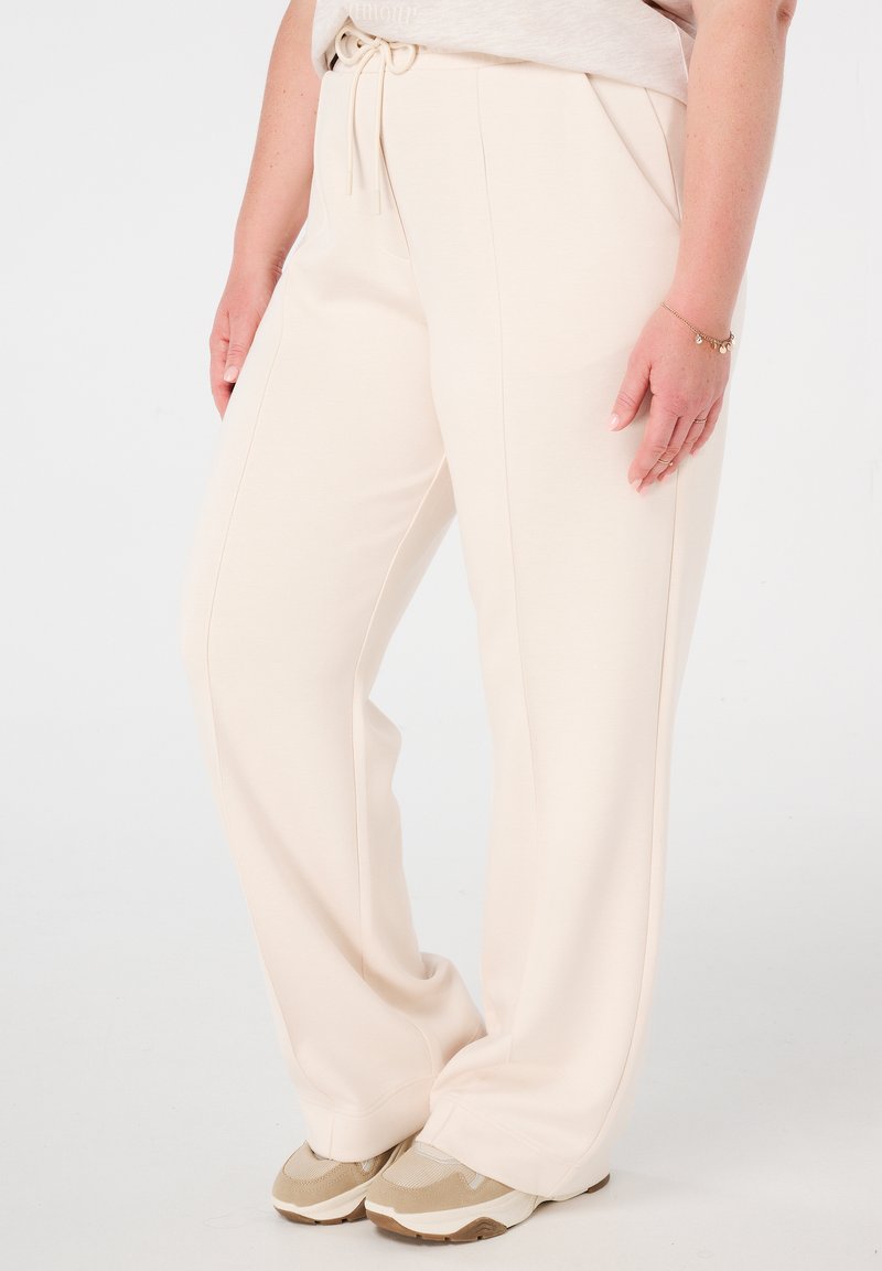 Beige wijde broek gemaakt van zachte stof, met een verstelbare tailleband en zijzakken, gecombineerd met tan kleurige sportschoenen.