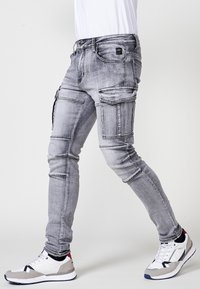 Grijze denim cargobroek met meerdere zakken, slim fit, vervaagde textuur en contrasterende stiksels, gecombineerd met lichtgewicht sneakers.