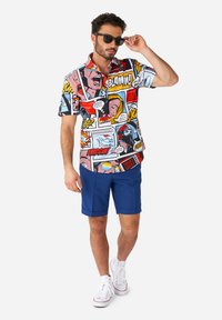 Short-sleeve, colorful comic-print shirt featuring speech bubbles and characters, paired with blue shorts and white sneakers.