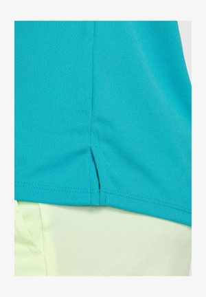 Top deportivo turquesa con un tejido texturizado, con una abertura lateral en el dobladillo, combinado con pantalones de un verde claro.
