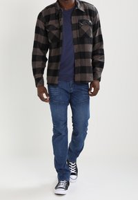 Svart och grå rutigt flanellskjorta, blå t-shirt, blå jeans och svarta sneakers. Två bröstfickor på flanellen. Avslappnad outfit.