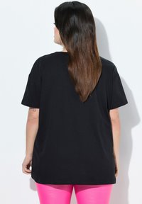 Sort t-shirt med afslappet pasform, korte ærmer og rund halsudskæring, parret med lyserøde leggings med høj talje.