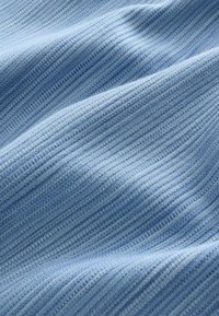 Tissu texturé bleu clair, présentant un motif en relief avec des variations subtiles de teinte et de tissage, créant un aspect doux et fluide.
