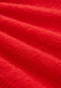 Miękka czerwona tkanina o puszystej fakturze, przedstawiona z bliska z delikatnymi fałdami i widocznymi włóknami.