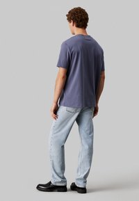 T-shirt a maniche corte in cotone viola tenue. La parte posteriore presenta un taglio dritto e un collo rotondo, abbinato a jeans in denim blu chiaro e stivali neri.