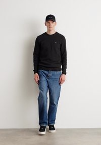 Svart hettegenser, blå jeans og svarte joggesko. Antrekket inkluderer en svart baseballcaps med logo. Enkelt, uformelt design.