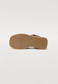 Infradito marrone con suola in gomma texturizzata, caratterizzata da un design piatto e una larga fascia sulla parte superiore. Finitura liscia, leggero.