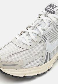 Nike Yomero 5 löparsko i ljusgrått, med överdel i mesh, vita accenter, vadderad tunga, texturerad sula och reflexdetaljer.