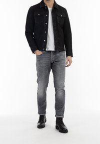 Musta denim-takki, jossa on napsautettavat napit, kaksi rintataskua, yhdistettynä harmaisiin farkkuihin ja mustiin nauhakenkiin, valkoista taustaa vasten.