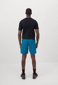 Black short-sleeve shirt, teal shorts, black shoes with red accents. Shorts are above the knee. Simple design, no visible patterns.