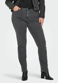 Sive traperice slim fit kroja, s prednjim džepovima, visokim strukom i suptilnim izbljeđenjem. Uparene s crnim čizmama s potpeticama.