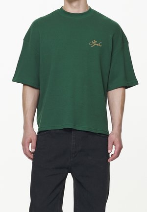 Zielony, oversize'owy t-shirt wykonany z fakturowanej tkaniny, z okrągłym dekoltem. Posiada krótkie rękawy i subtelne złote logo na piersi.