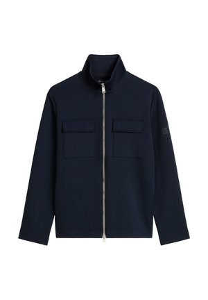 Marineblauwe jas met rits en hoge kraag, twee borstzakken en lange mouwen. Gemaakt van zacht materiaal, met vlakke naden en minimale accenten.