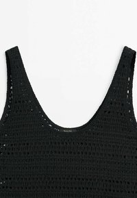 Haut débardeur en crochet noir sans manches avec encolure dégagée et motif texturé sur fond blanc.