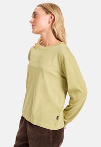 T-shirt a maniche lunghe verde chiaro con collo a giro, tessuto morbido e dettaglio del logo di dimensioni ridotte. Abbinato a pantaloni in corduroy scuri.