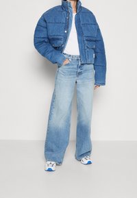 Niebieska pikowana kurtka jeansowa z wysokim kołnierzem, przednimi kieszeniami i krótkim krojem; w zestawie z jasnoniebieskimi szerokimi spodniami dżinsowymi i białymi trampkami.