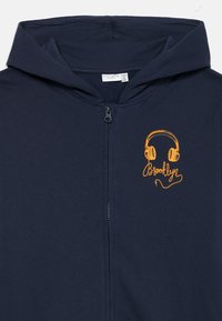 Marine zip-up hættetrøje lavet af blødt stof, med et orange hovedtelefon grafik og "Brooklyn" tekst, samt en snøre i hætten.