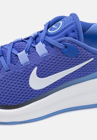 Vijolična Nike tekaška čevelj z belim swoosh logotipom, mrežasto zgornji del, modre vezalke in bela srednja podloga na svetli podlagi.