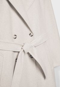 Lys grå uldblandingsfrakke med belted talje, dobbeltknaplukning og spids krave. Blød tekstur og skræddersyet design.
