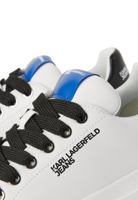 Bílé kožené tenisky s černými tkaničkami, modro-černým patním poutkem a logem "Karl Lagerfeld Jeans" na boku.